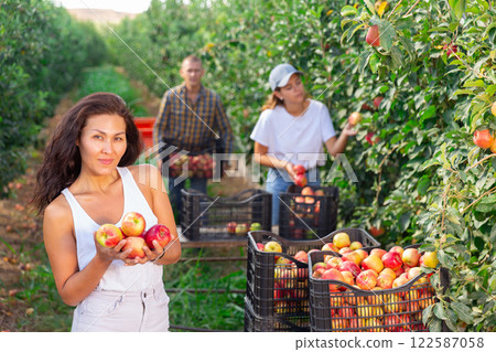 Smiling Asian woman posing in garden with ripe apple in hands Smiling Asian woman posing in garden with ripe apple in hands 122587058
