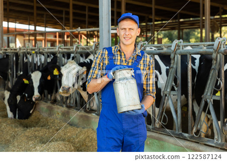 Positive farmer carrying milk can in open stall with cows Positive farmer carrying milk can in open stall with cows 122587124