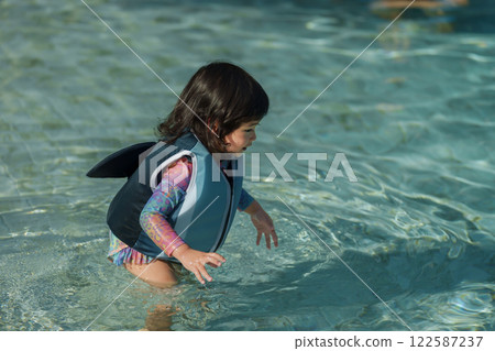 happy toddler baby girl in life jacket playing water in swimming pool 122587237