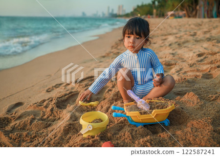 happy toddler baby girl playing sand toy on sea beach in Pattaya, Thailand happy toddler baby girl playing sand toy on sea beach in Pattaya, Thailand 122587241
