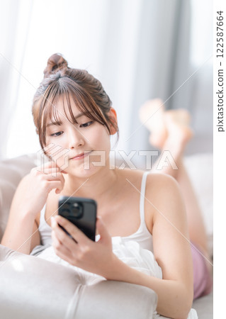 一位年輕女子在家中，手裡拿著智慧型手機，思考著如何回复 122587664