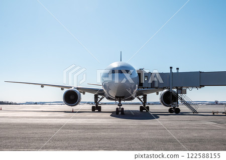 Front view of the white wide body passenger airplane at the boarding bridge on the airport apron 122588155