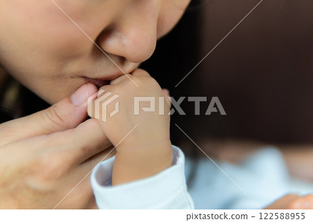 A caring Asian mom kisses her newborn baby's hand closeup. 122588955