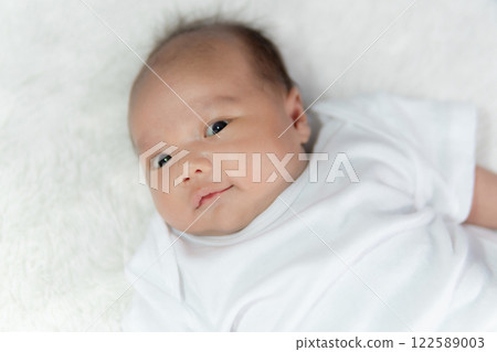 Close-up of a happy smiling baby on a white cotton bed in a bright bedroom. Close-up of a happy smiling baby on a white cotton bed in a bright bedroom. 122589003