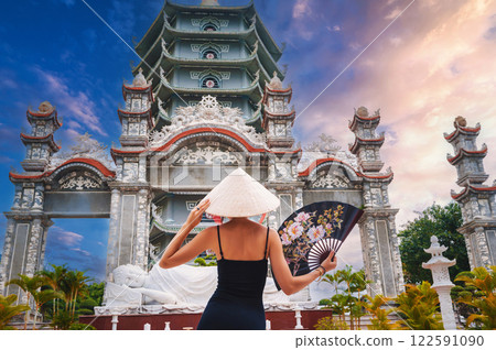 back of a female tourist in a Vietnamese Non La hat at Da Nang pagoda in Vietnam. Travel and tourism in Asia back of a female tourist in a Vietnamese Non La hat at Da Nang pagoda in Vietnam. Travel and tourism in Asia 122591090