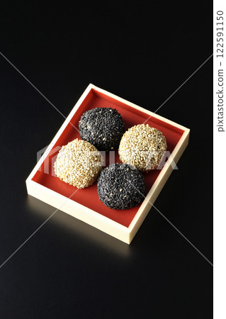 White and black sesame balls photographed against a black background 122591150