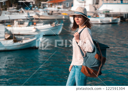 Beautiful girl with a backpack enjoys a view on the seashore. Beautiful girl with a backpack enjoys a view on the seashore. 122591304