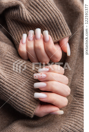 Woman showing stylish white manicure on brown knitted sweater 122591377