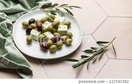 White plate presenting green and black olives with feta cheese cubes and olive branches White plate presenting green and black olives with feta cheese cubes and olive branches 122591392