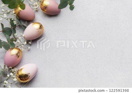 Elegant easter eggs with gold leaf and eucalyptus leaves creating a border on gray background 122591398