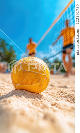 close up of yellow volleyball on sandy beach with players in background 122591789