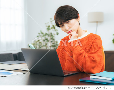 A middle-aged woman worried while looking at her smartphone and laptop A middle-aged woman worried while looking at her smartphone and laptop 122591799