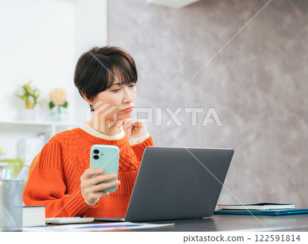 A middle-aged woman worried while looking at her smartphone and laptop A middle-aged woman worried while looking at her smartphone and laptop 122591814