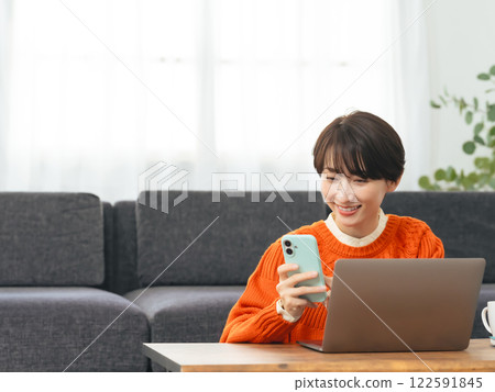 Woman using laptop and smartphone in living room Woman using laptop and smartphone in living room 122591845