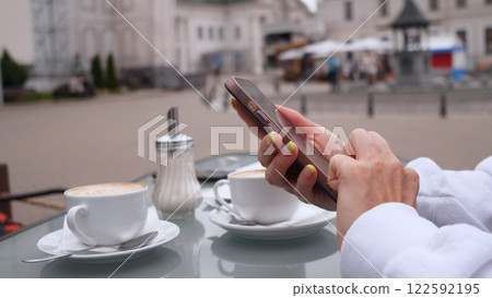 Enjoying a relaxing moment with coffee while using a smartphone in a cozy setting, outdoors 122592195