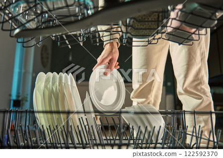 Person loading plates into dishwasher rack 122592370
