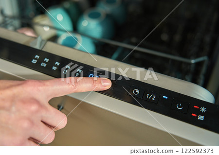 Finger pressing button on dishwasher control panel 122592373