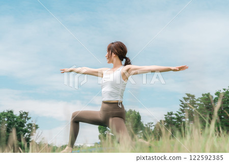 A woman meditating, doing yoga, stretching and pilates in the grassland (healthcare and diet) 122592385