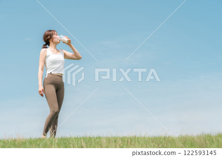 Woman drinking protein/EAA drink during exercise (blue sky) Woman drinking protein/EAA drink during exercise (blue sky) 122593145