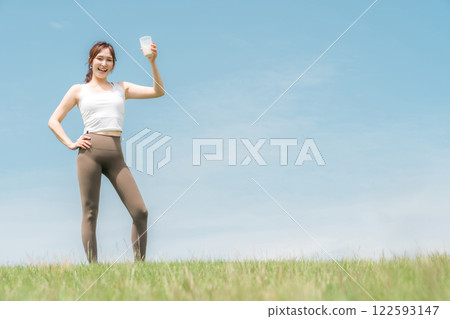 Woman drinking protein/EAA drink during exercise (blue sky) Woman drinking protein/EAA drink during exercise (blue sky) 122593147