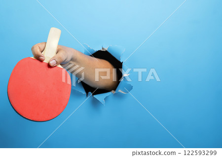 Human hand holding table tennis paddle through ripped paper. Mockup or Copy space. Concept of sport 122593299