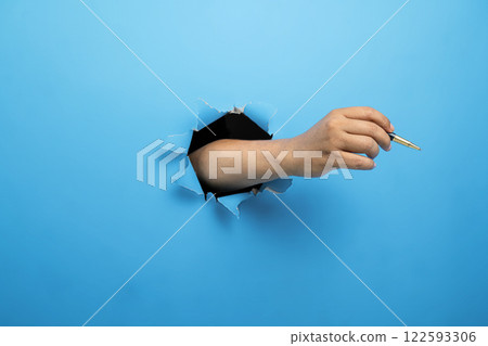 Human hand holding ballpoint pen through ripped paper. Mockup or Copy space. Concept of business, signature, communication, or handwriting Human hand holding ballpoint pen through ripped paper. Mockup or Copy space. Concept of business, signature, communication, or handwriting 122593306