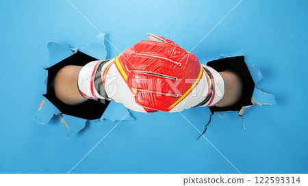 Human hand wearing goalkeeper gloves through ripped paper. Mockup or Copy space. Concept of sport Human hand wearing goalkeeper gloves through ripped paper. Mockup or Copy space. Concept of sport 122593314