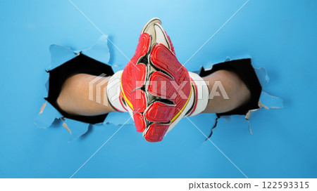 Human hand wearing goalkeeper gloves through ripped paper. Mockup or Copy space. Concept of sport 122593315