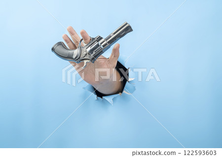 Human hand holding handgun through ripped paper. Hand gestures. Mockup or Copy space. Aiming weapons, war, crime, or violence Human hand holding handgun through ripped paper. Hand gestures. Mockup or Copy space. Aiming weapons, war, crime, or violence 122593603