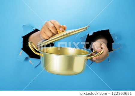 A human hand is holding a saucepan through ripped paper. Hand gestures to serve food. Mockup or Copy space A human hand is holding a saucepan through ripped paper. Hand gestures to serve food. Mockup or Copy space 122593651
