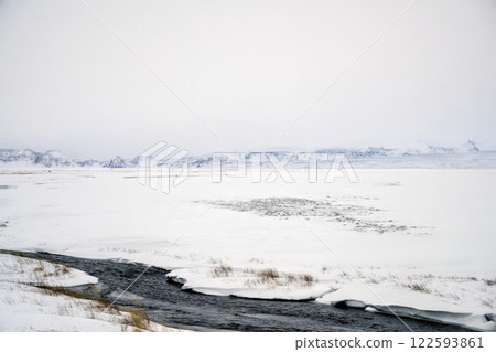 Landscape view of river flow with snow covered fields and mountain ranges in Iceland. Nature, travel, winter background, or wallpaper 122593861