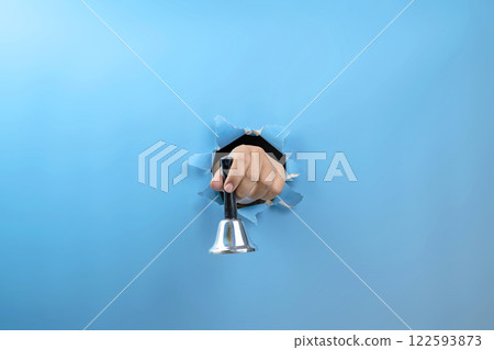 Human hand holding ringing handbell through ripped paper. Hand gestures. Mockup or Copy space. Traditional hand bell for ringing or calling attention Human hand holding ringing handbell through ripped paper. Hand gestures. Mockup or Copy space. Traditional hand bell for ringing or calling attention 122593873