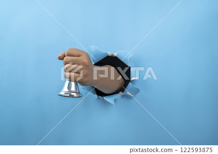 Human hand holding ringing handbell through ripped paper. Hand gestures. Mockup or Copy space. Traditional hand bell for ringing or calling attention 122593875