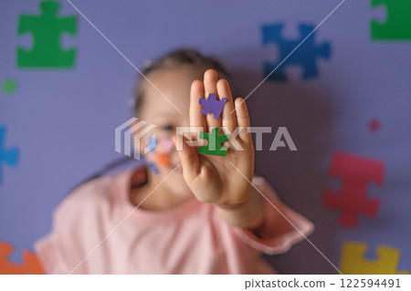 Colored puzzles in a child's hand close-up on a purple background. A concept on education and autism. Colored puzzles in a child's hand close-up on a purple background. A concept on education and autism. 122594491