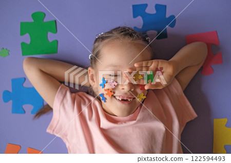 Pretty Girl holds pieces of multi colored puzzles in hand, laughing and covering eyes with palm. Education and development of children of school and preschool age. Pretty Girl holds pieces of multi colored puzzles in hand, laughing and covering eyes with palm. Education and development of children of school and preschool age. 122594493