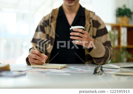 Creative man taking notes in a notebook and sipping coffee at workplace 122595915