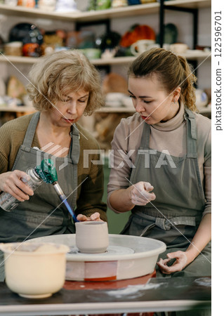Mentor teaches pottery fundamentals, demonstrating sculpting skills on an electric wheel Active aging concept, retired woman explores pottery as a new passion using a spinning wheel 122596701