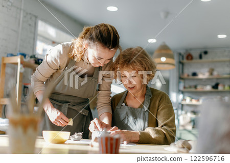 Elderly Caucasian woman learns pottery at a creative workshop with a young mentor. Two women work together with clay, developing skills and enjoying the artistic process 122596716