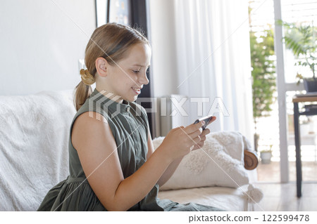 Happy young girl using the phone, playing the game, sitting on sofa at cozy home. Happy young girl using the phone, playing the game, sitting on sofa at cozy home. 122599478
