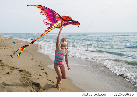 Girl Running with Dragon Kite on Beach Girl Running with Dragon Kite on Beach 122599650
