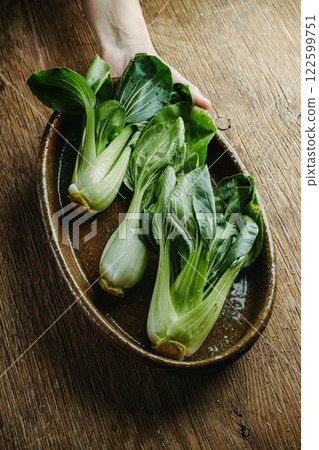 man grabbing a casserole with some raw bok choys 122599751
