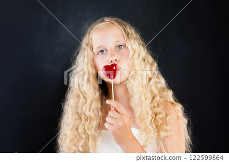 Pretty young child girl with blond hair and blue eyes holding red heart  122599864