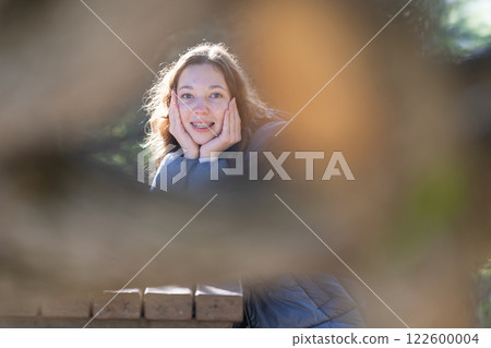 Teenager girl with braces smiling in park behind branches Teenager girl with braces smiling in park behind branches 122600004