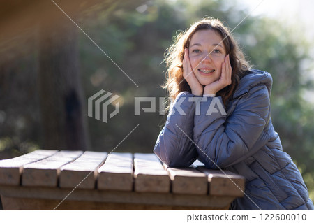 Smiling teenager with braces leaning on wooden table in park Smiling teenager with braces leaning on wooden table in park 122600010