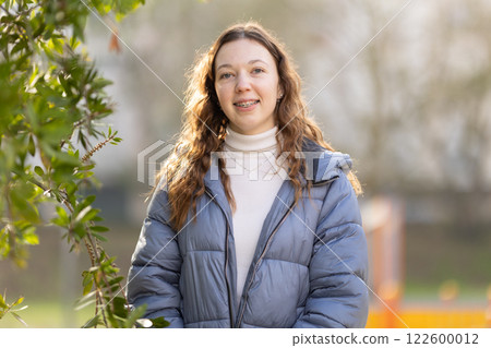 Young woman smiling outdoors, wearing braces and winter clothes 122600012