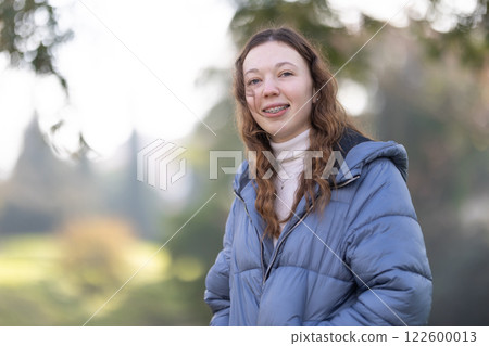 Happy student wearing dental braces is posing in a park during winter Happy student wearing dental braces is posing in a park during winter 122600013