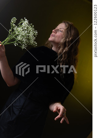 A beautiful mature woman holds a white flowers on a dark studio background. A beautiful mature woman holds a white flowers on a dark studio background. 122600123