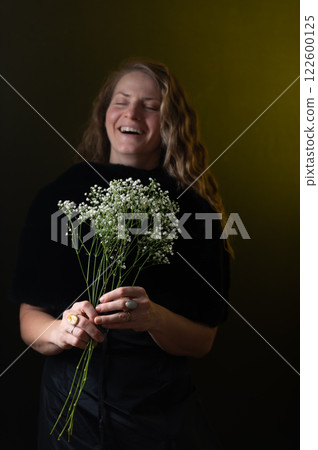 A beautiful mature woman holds a white flowers on a dark studio background. 122600125