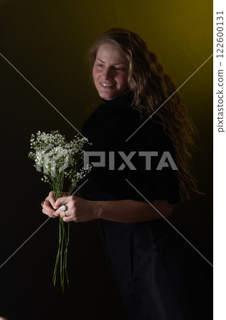 A beautiful mature woman holds a white flowers on a dark studio background. A beautiful mature woman holds a white flowers on a dark studio background. 122600131