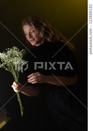 A beautiful mature woman holds a white flowers on a dark studio background. 122600182